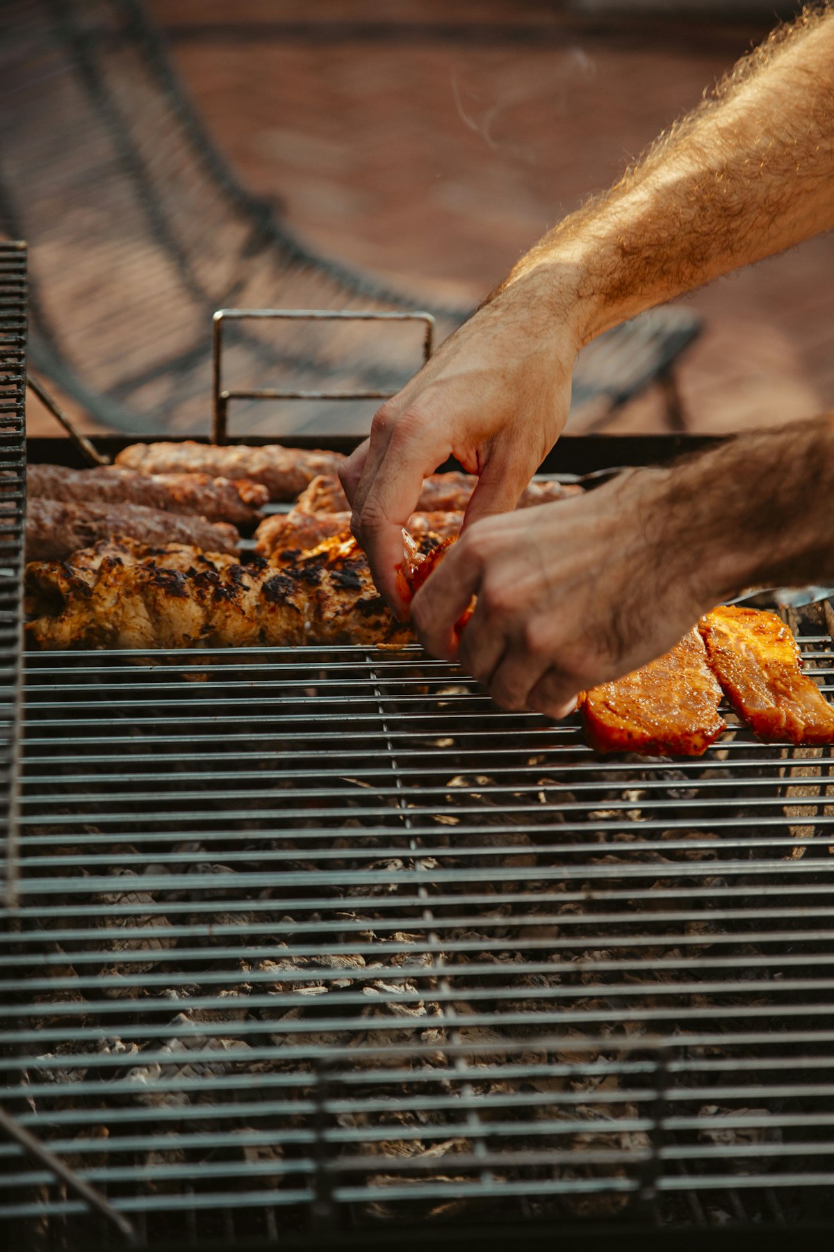 A pitmaster grilling meat outdoors with smoke rising
